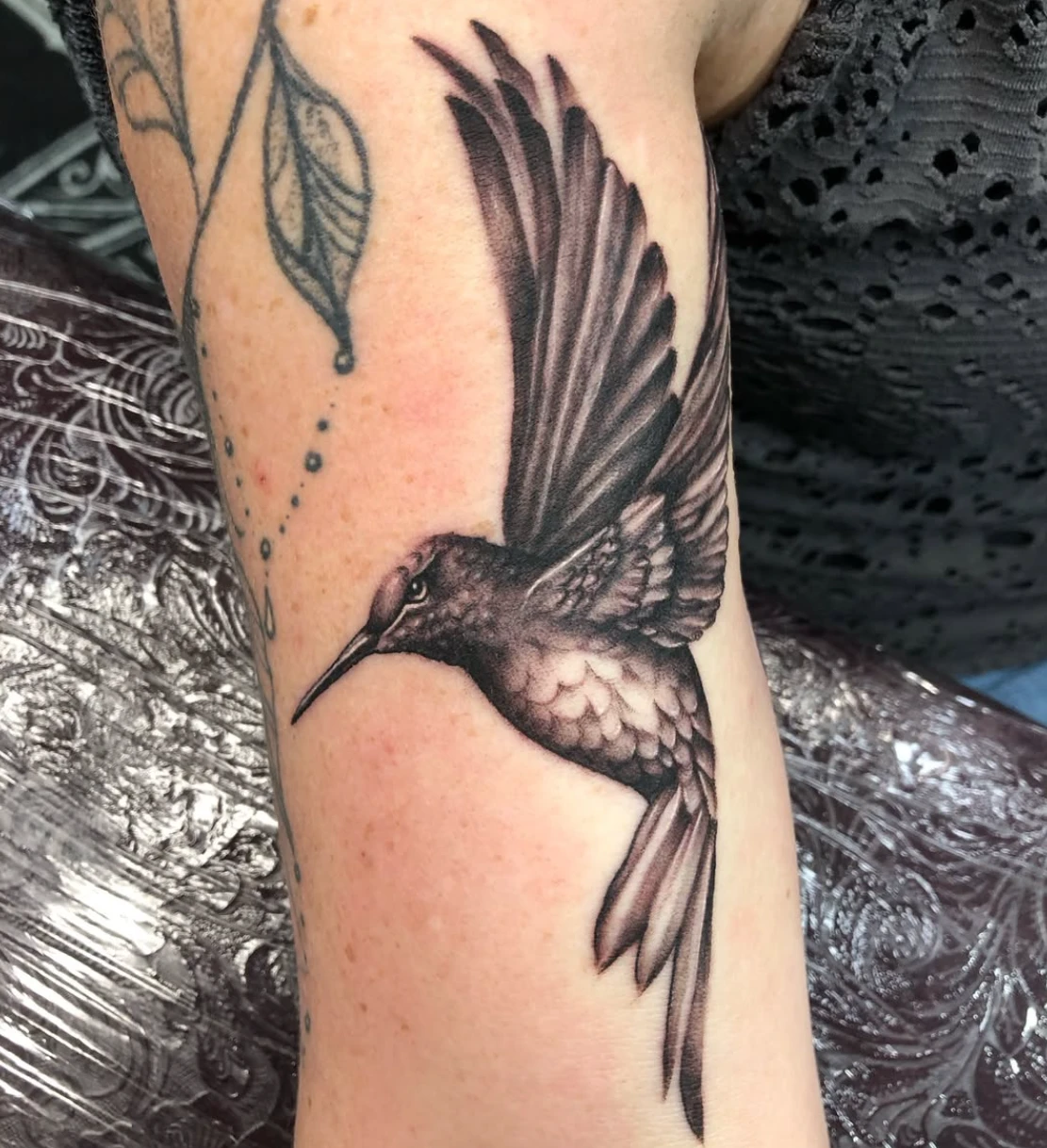 Black and grey realistic hummingbird in flight tattooed on an upper arm by Adam Harper