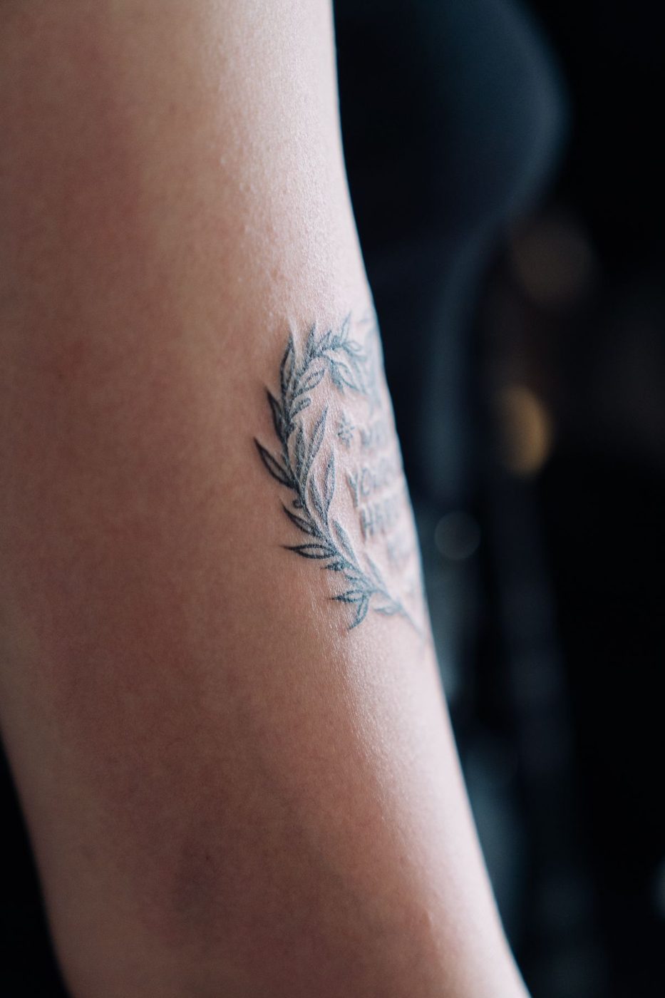 Fine-line leafy wreath tattoo on a forearm