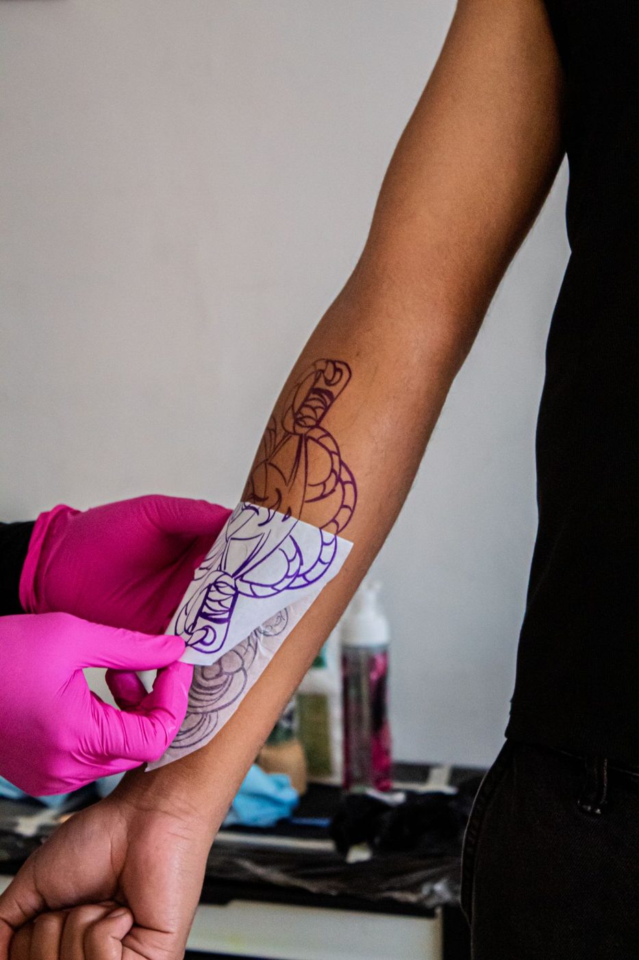 Gloved hands pressing a tattoo stencil onto a forearm