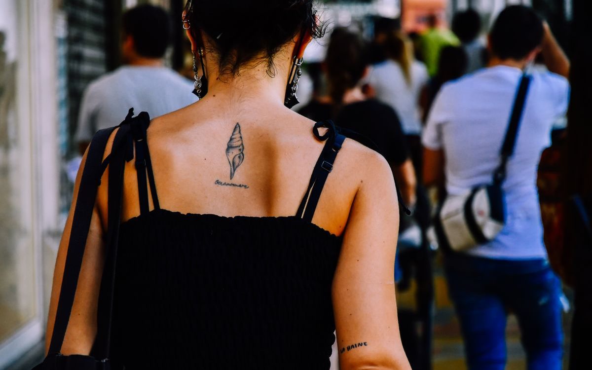 Woman seen from behind in a city crowd with a small tattoo between her shoulder blades