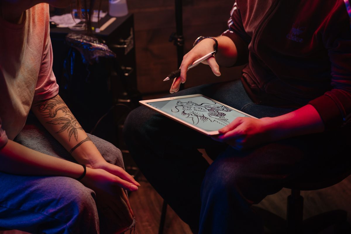 Tattoo artist consulting with a client and sketching a design in studio