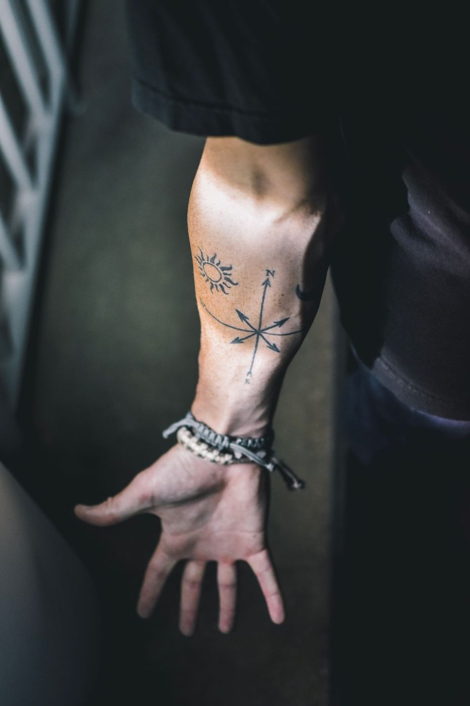 Forearm with a small line tattoo and a beaded bracelet, hand open