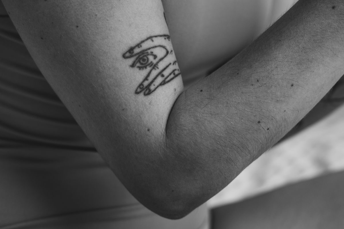 Small black line tattoo of a hand with an eye on an upper arm, in black and white