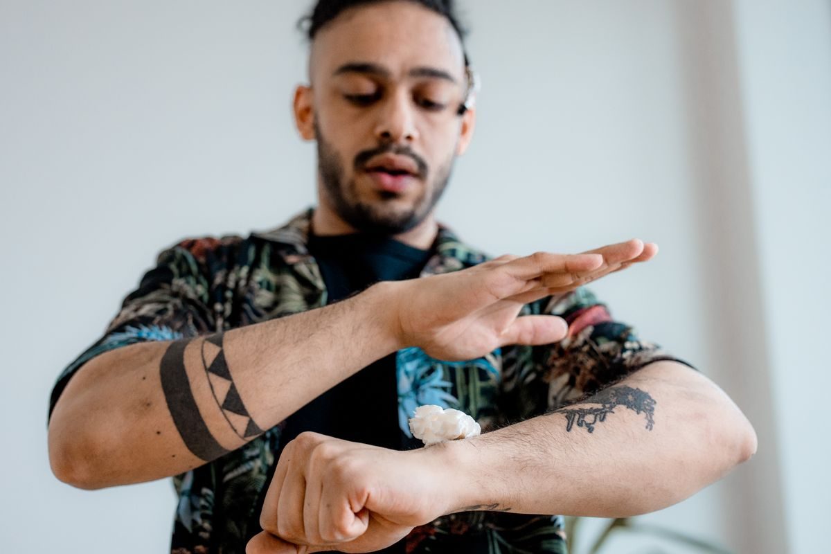 Man with tattooed forearms squeezing lotion from a bottle onto his forearm