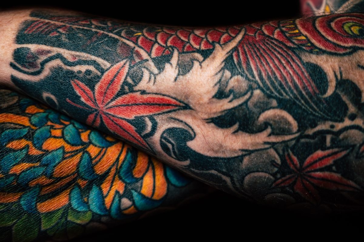 Close-up of a Japanese-style tattoo sleeve with red maple leaves, waves and bright flowers
