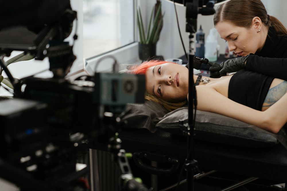 A tattoo artist filming a tattoo session with a video camera set up in studio